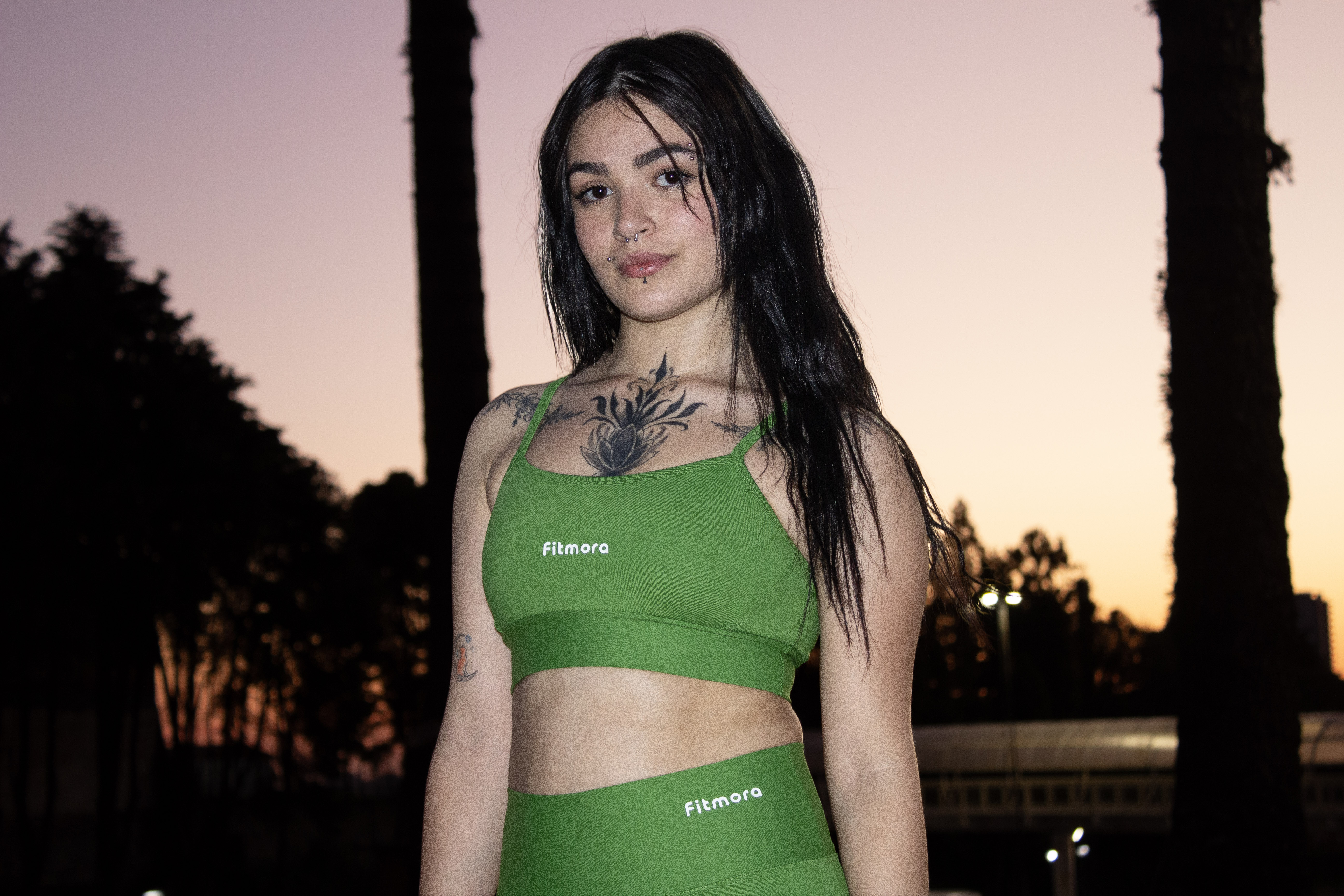 Modelo de frente vestindo top e legging verdes Fitmora ao entardecer