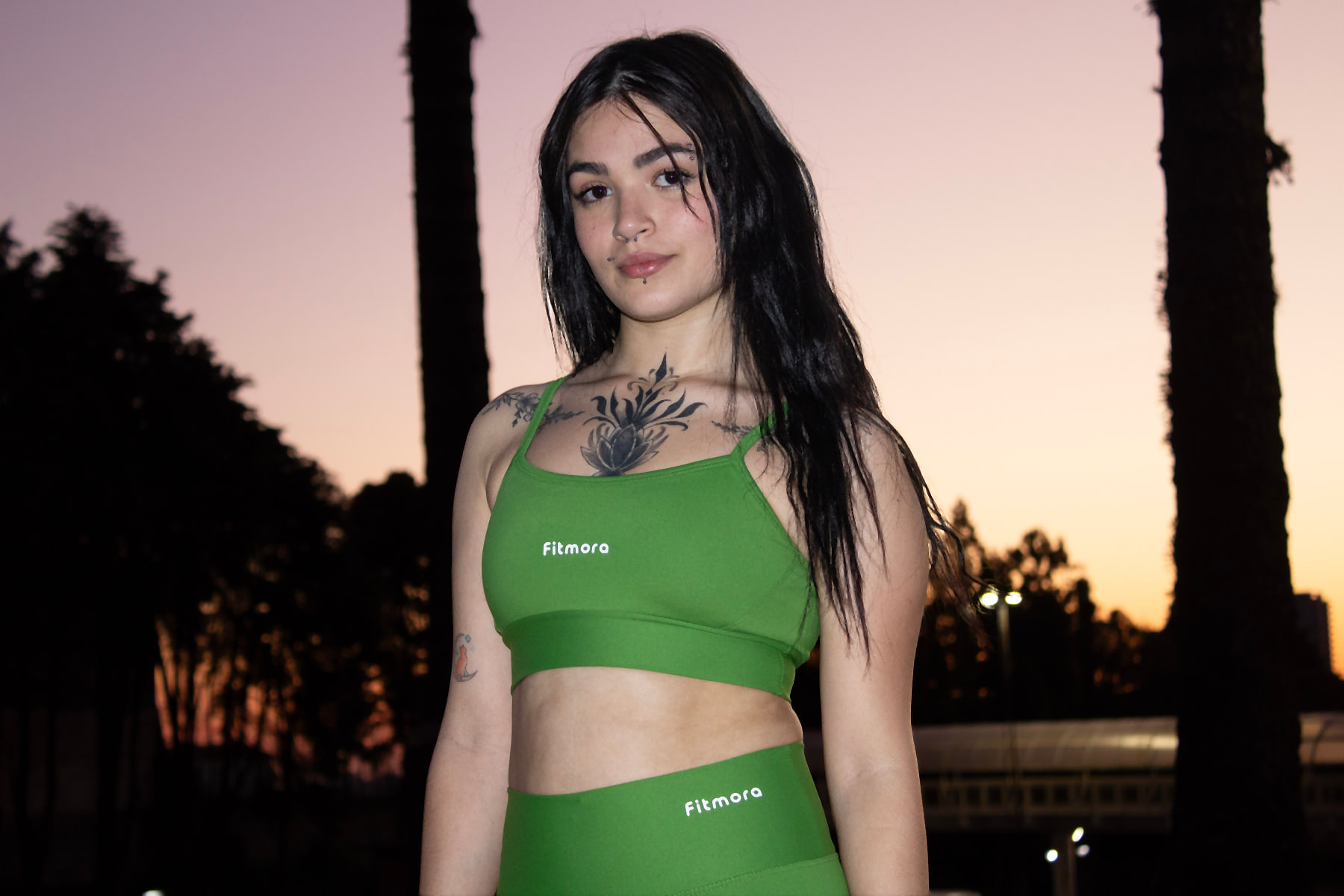 Modelo com top e legging verdes Fitmora ao pôr do sol
